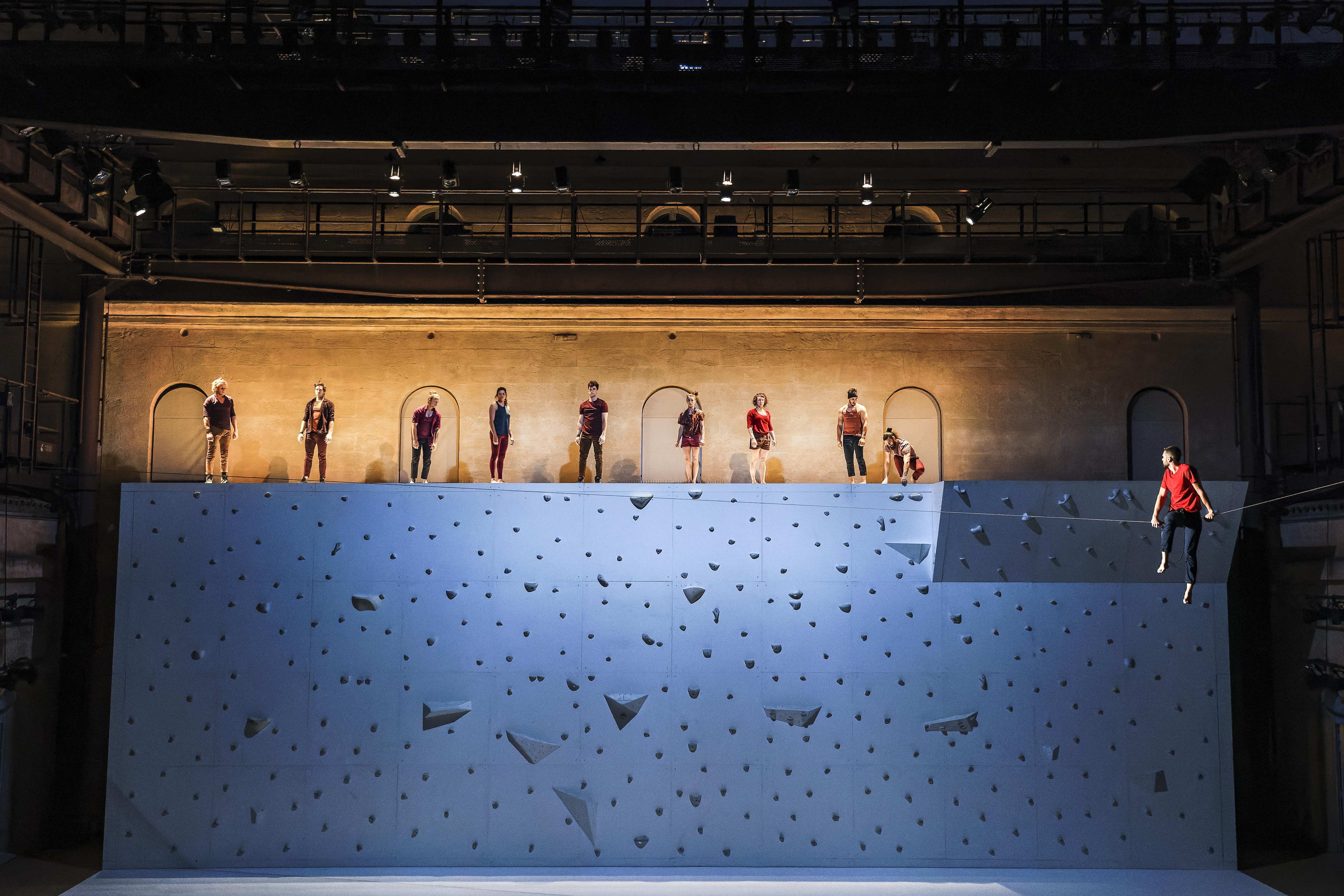 Dancers on top of a climbing wall behind a stage