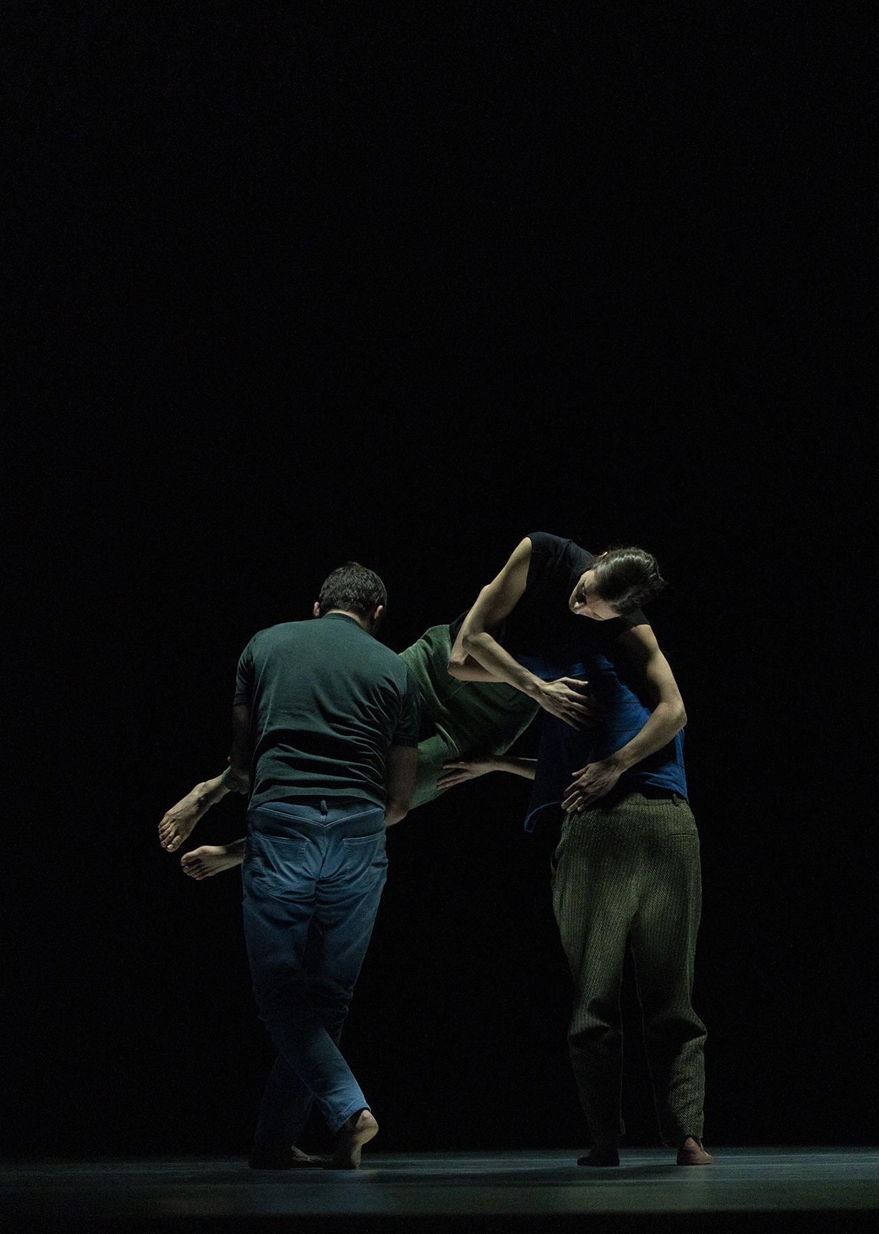 Two dancers facing upstage carrying a third dancer turned to the audience