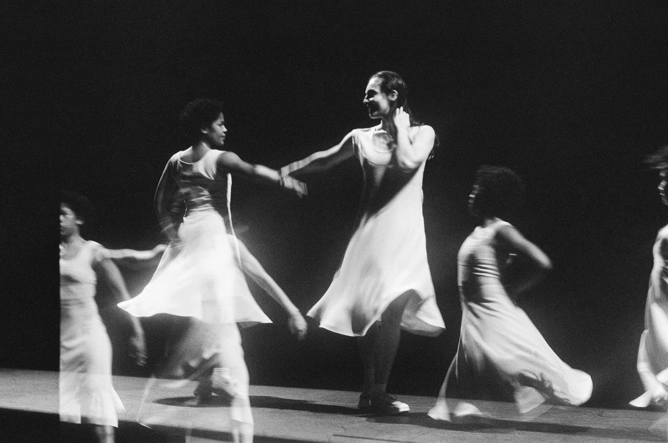 Dancers in white dresses against a black background