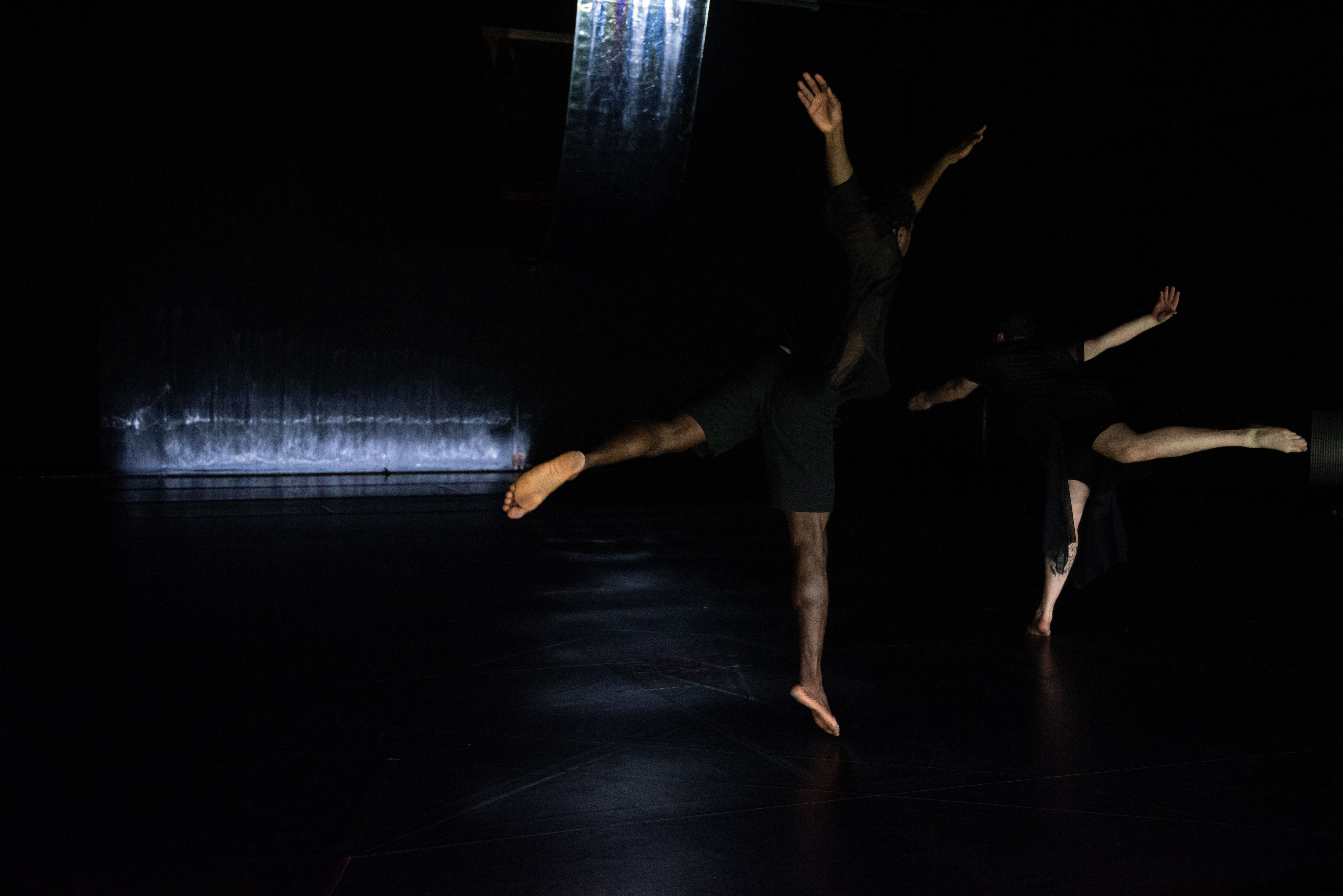 Two dancers jumping on a dark stage
