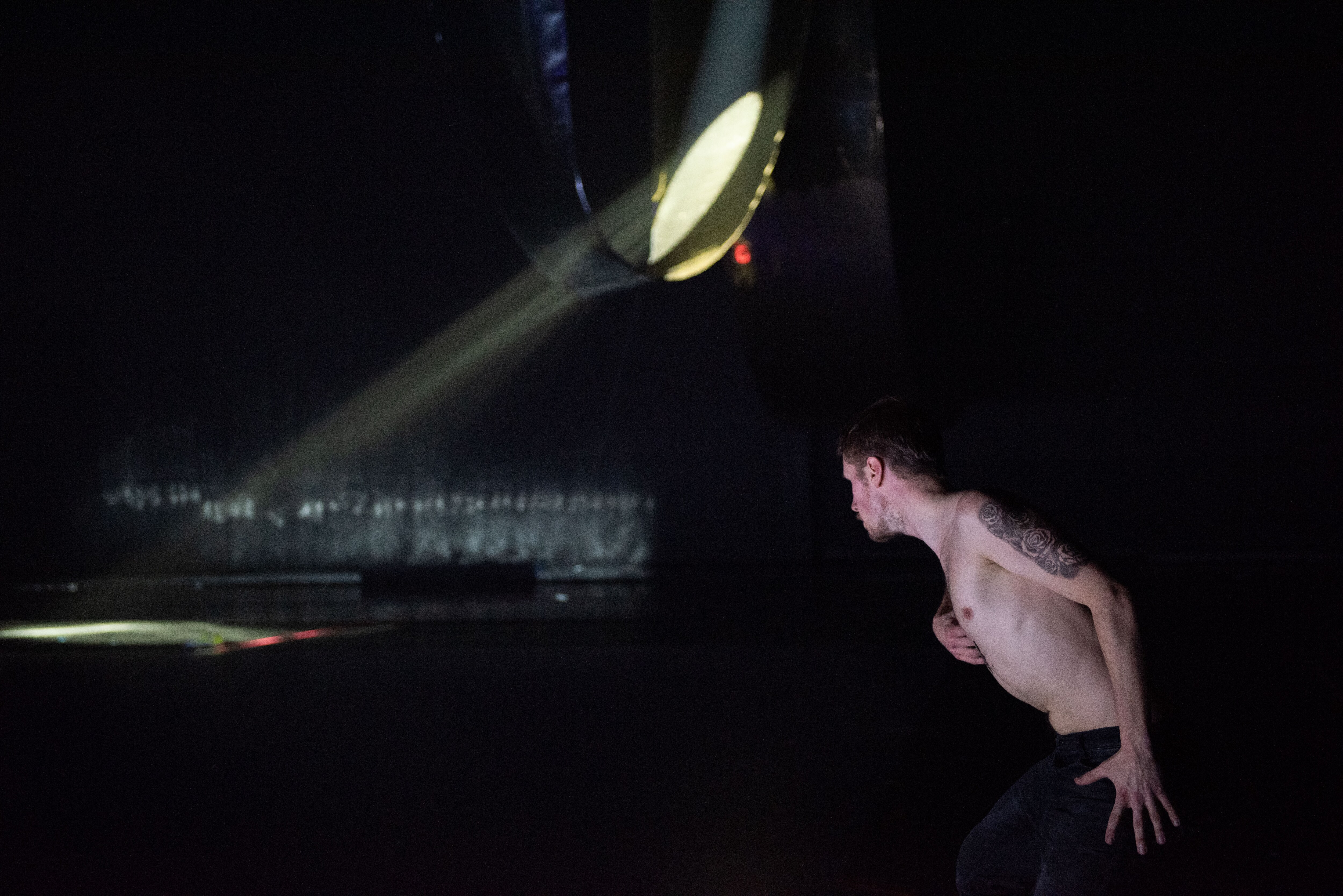 一位舞者在黑暗舞台上，面对一个散发出一束光线的建筑物