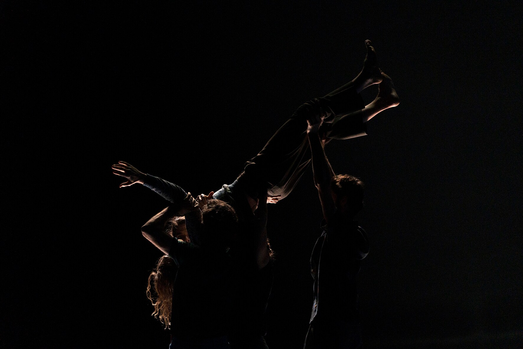 黑暗的舞台上，舞者们将其中一位舞者高举到空中
