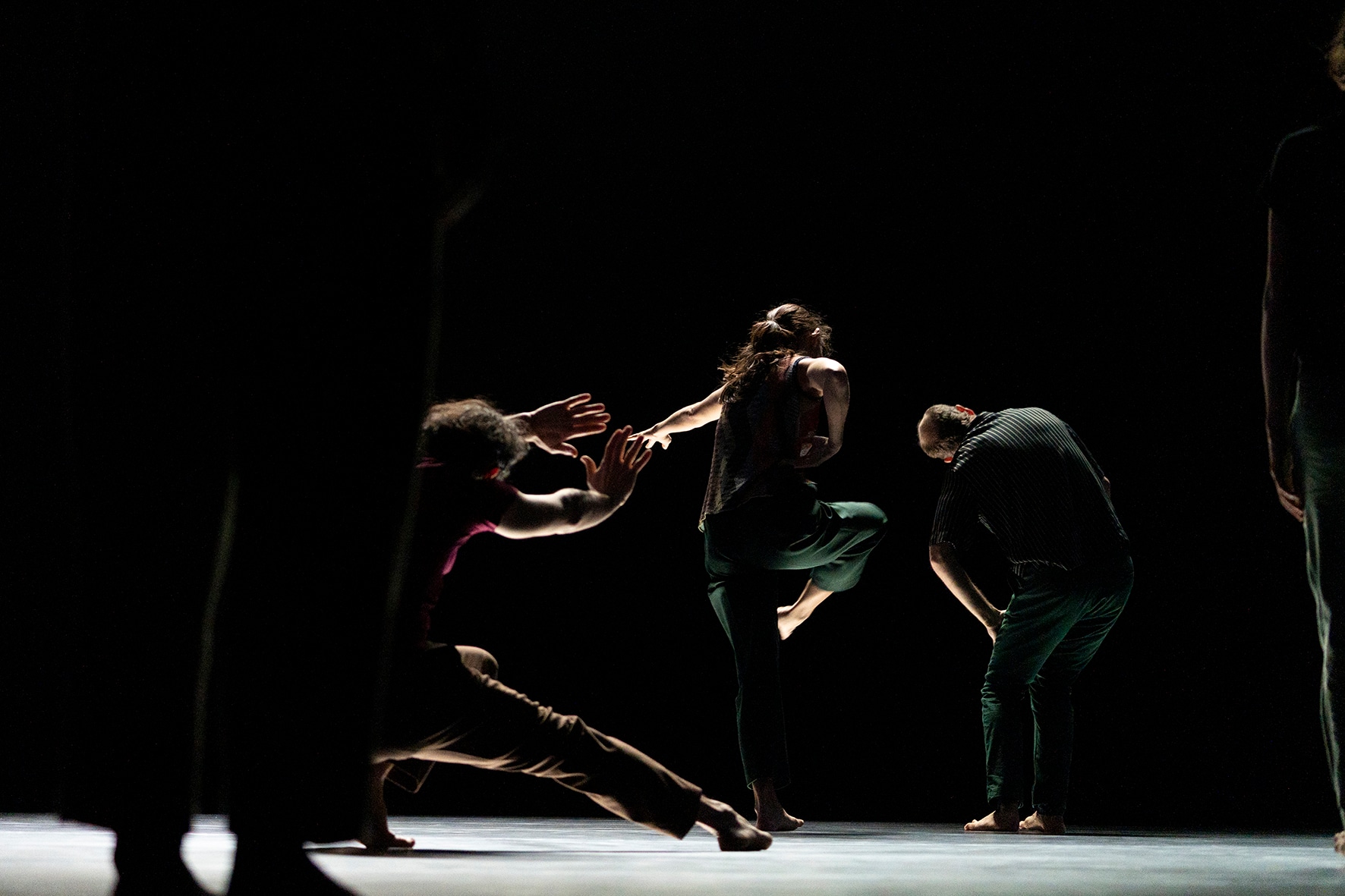 Trois danseurs en action sur en scène sombre devant un danseur