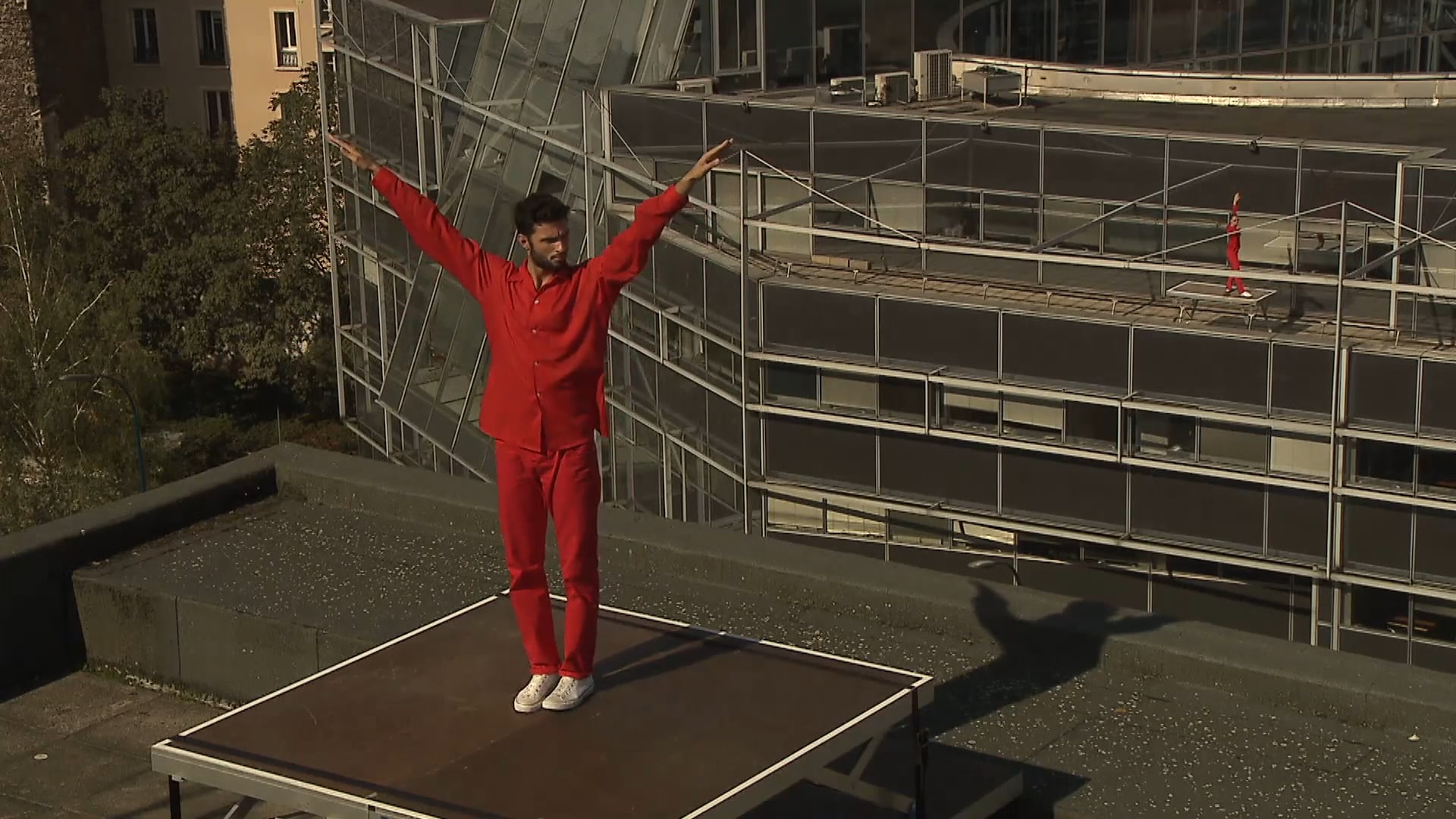Dancer in red on a roof with their arms pointing up 