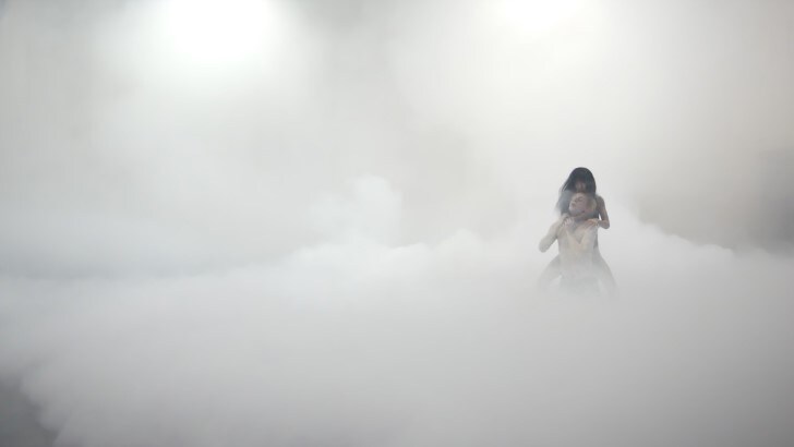 Woman strangling a man in the middle of a stage covered in mist