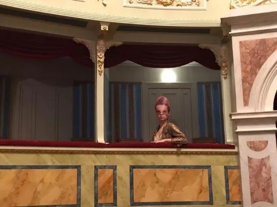 femme masquée assise, un bras posé sur la rambarde d’une loge de théâtre