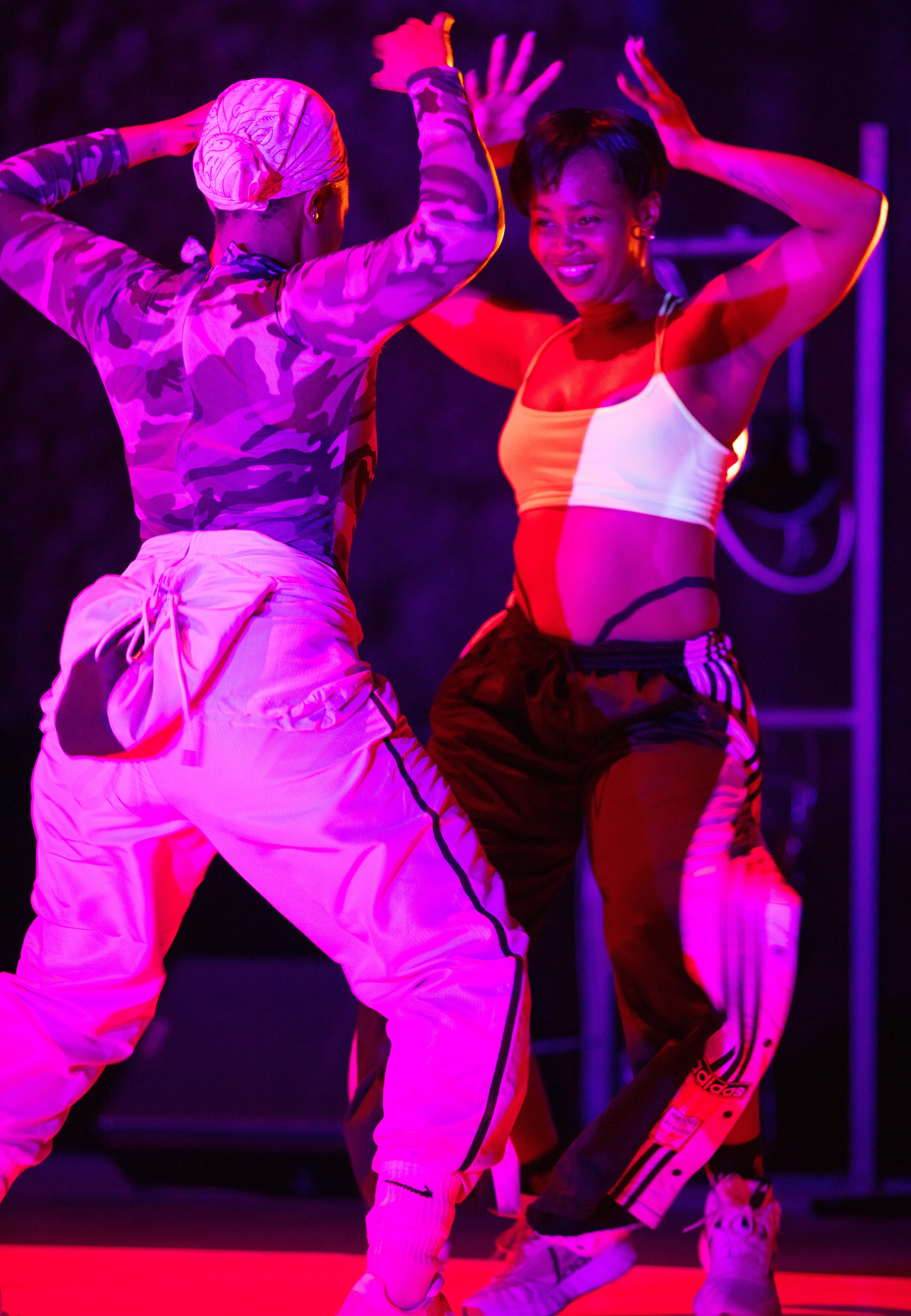 Two smiling dancers face each other, arms raised above their heads.