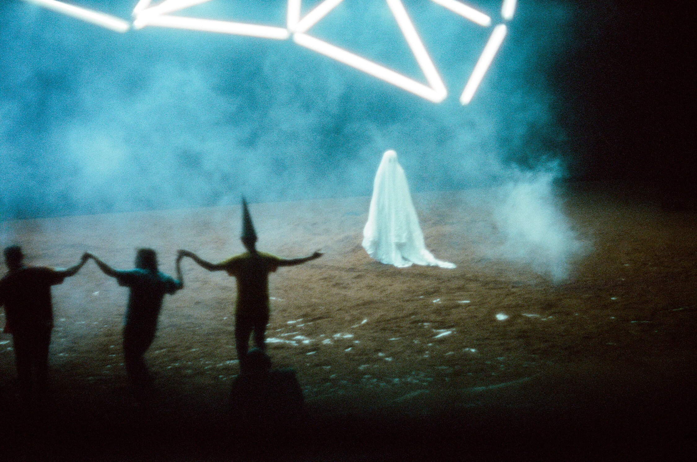 Dancer covered with a white sheet and three dancers holding hands in a cloud of smoke