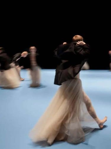 Dancers wearing pale pink long tutus and black jackets are walking