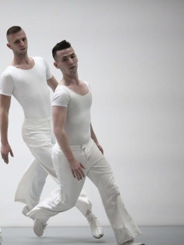 Four dancers dressed in white run on a white stage.