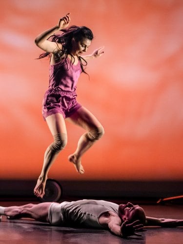 A dancer jumping, with a man lying on his back beneath her