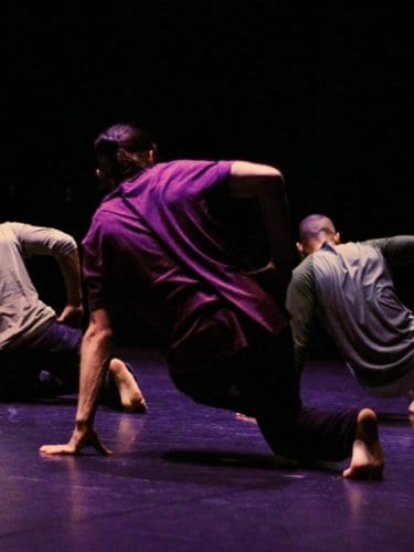 Three dancers seen from the back executing the same move on the floor