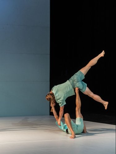 Dancers in light-colored outfits performing lifts and acrobatic figures on stage