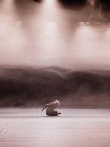 Dancer sitting in mist, under spotlights