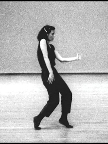 black and white picture of a dancer in black performing on an empty stage