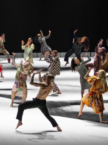 groupe de danseurs en costumes colorés et variés sur une scène blanche et noire, en pleine performance