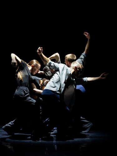 groupe de danseurs sur une scène noire, dans une pose dynamique