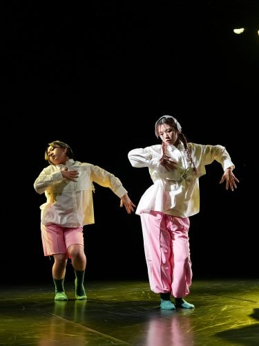4 dancers dressed in white tops and pink pants standing with their arms bent at right angles