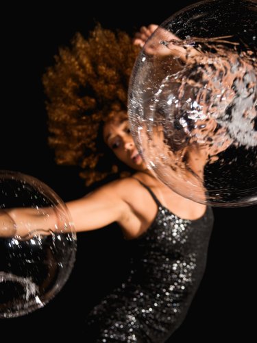 Une femme portant une robe pailletée danse avec des bulles. 