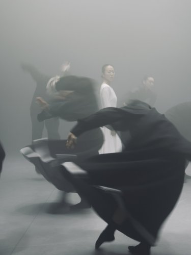 Danseurs en tenue noire  en mouvement tournant autour d'une danseuse dans une tenue blanche. 