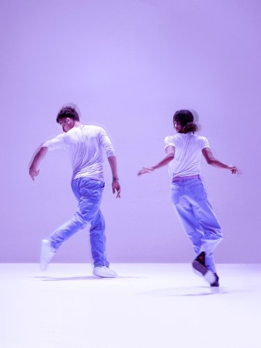 Deux danseurs de dos en mouvement, avec un fond mauve.