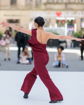 Danseuse en tenue bordeaux, vue de dos, les bras tendus, dançant en extérieur