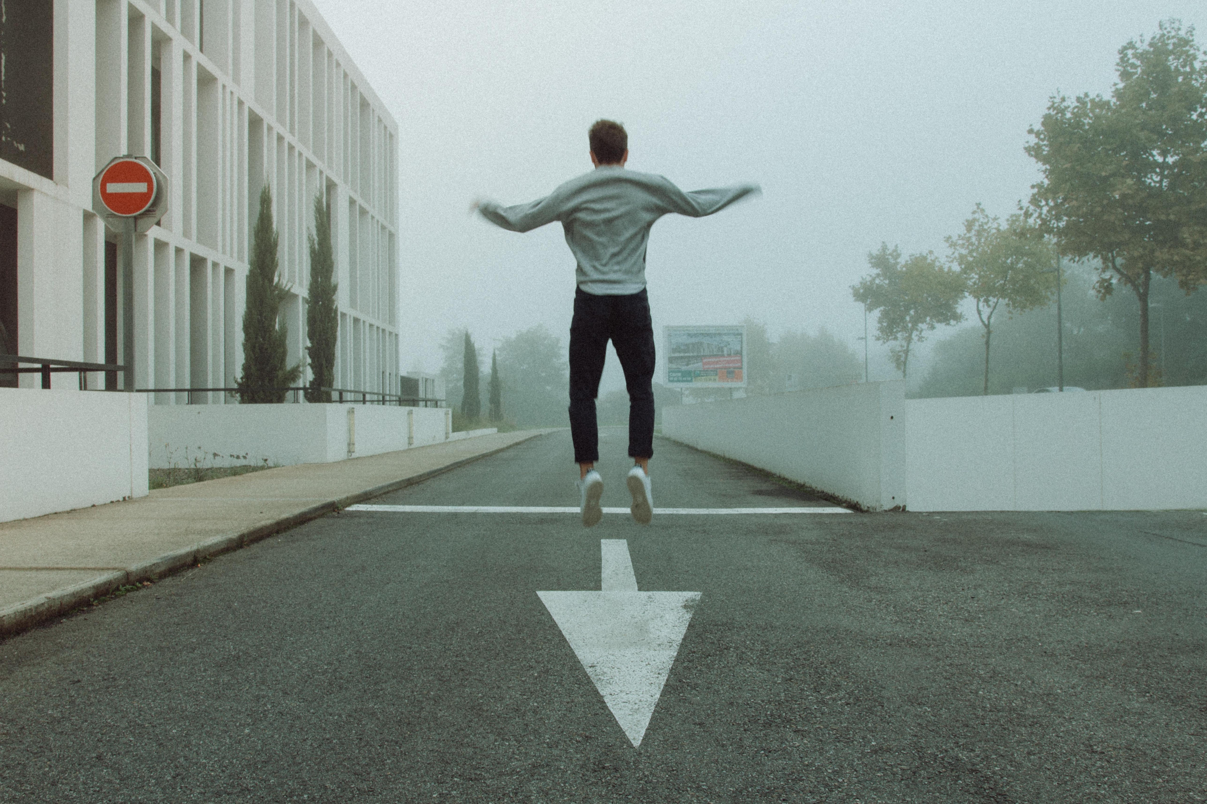 Back-facing man jumping at the end of a one-way street