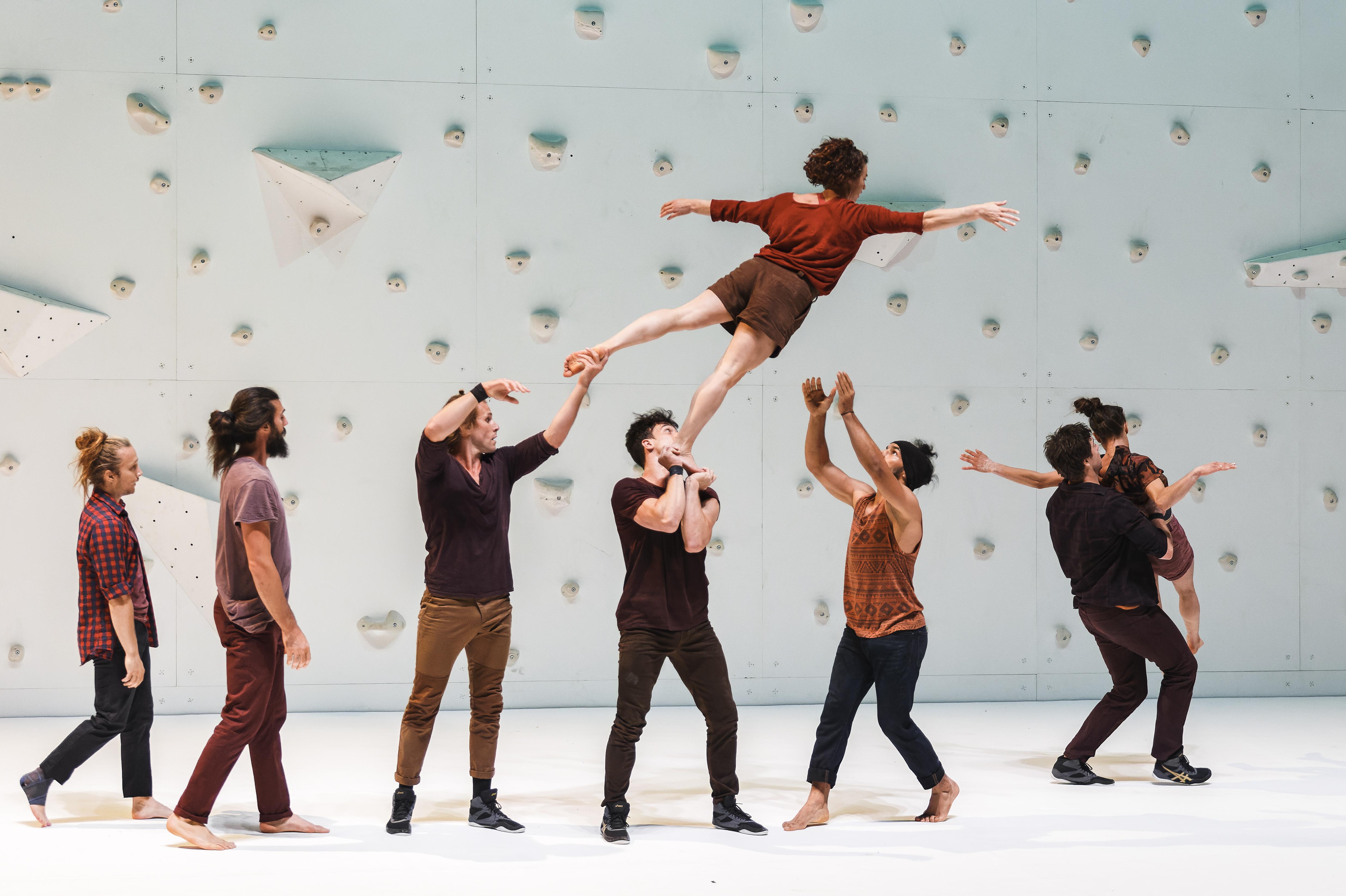 Dancers in front of a climbing wall balancing a dancer up in the air 