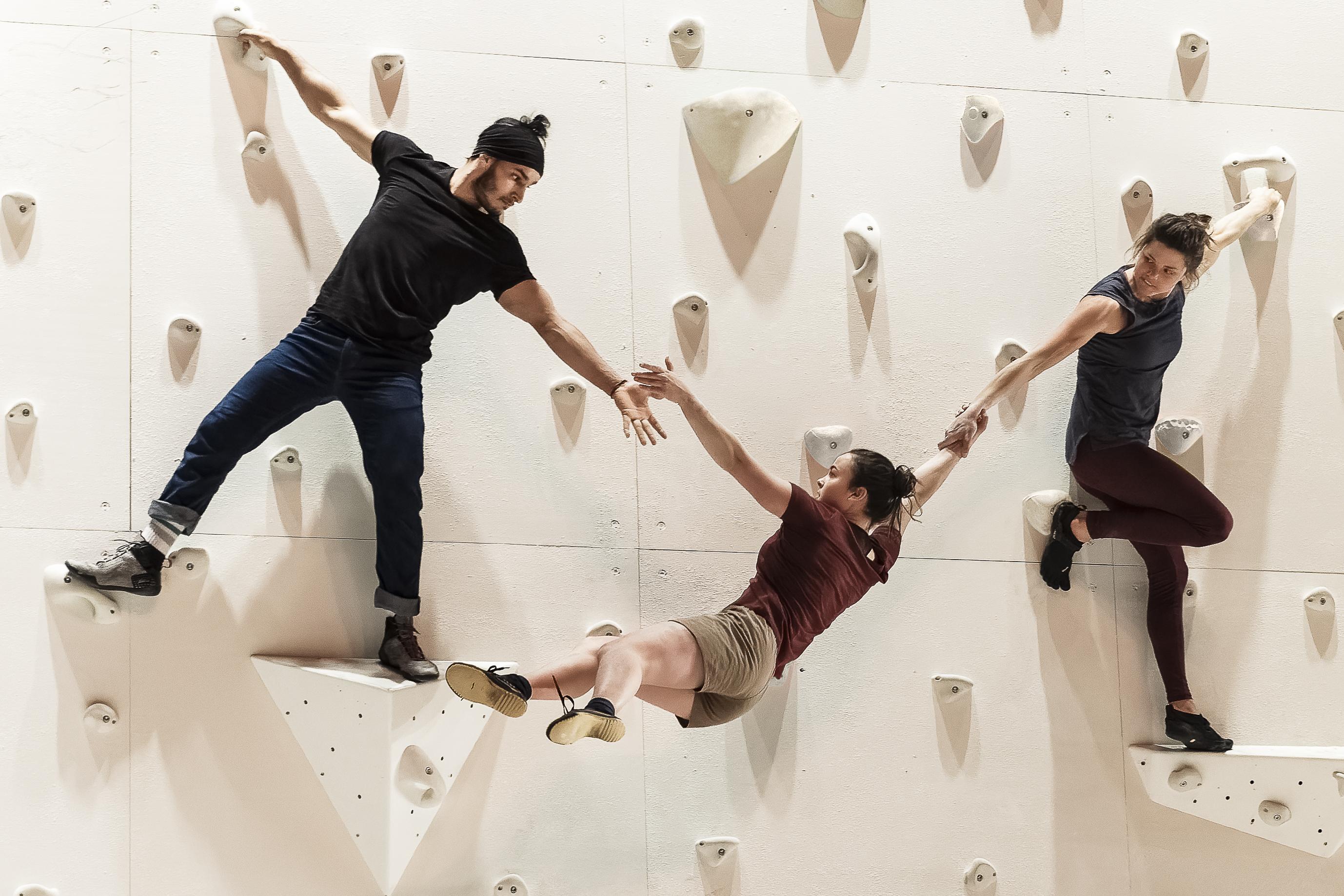 两位舞者攀爬白墙，同时将另一位舞者高举在空中