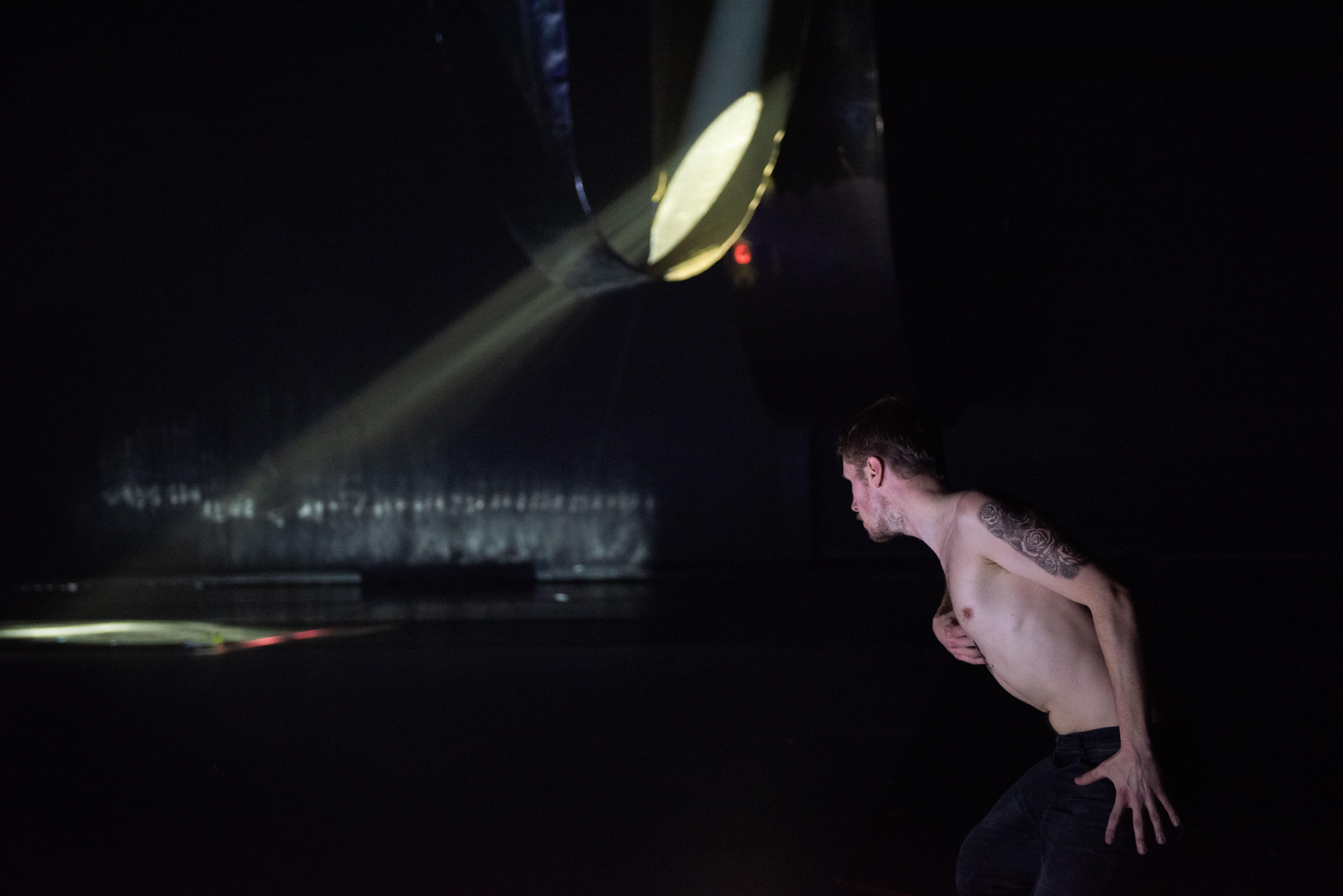 A dancer on a dark stage approaching a structure diffusing a ray of light 