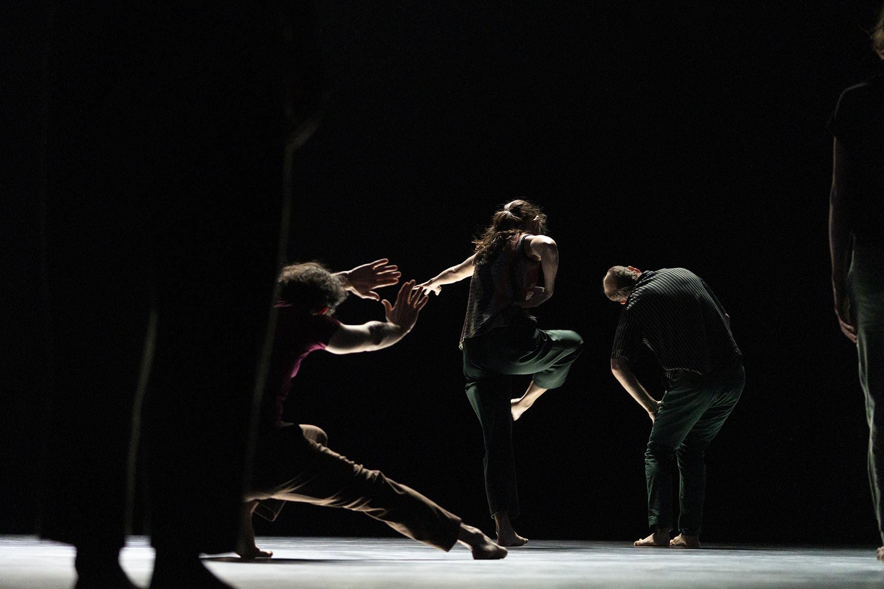 Three dancers in action on stage in front of another dancer