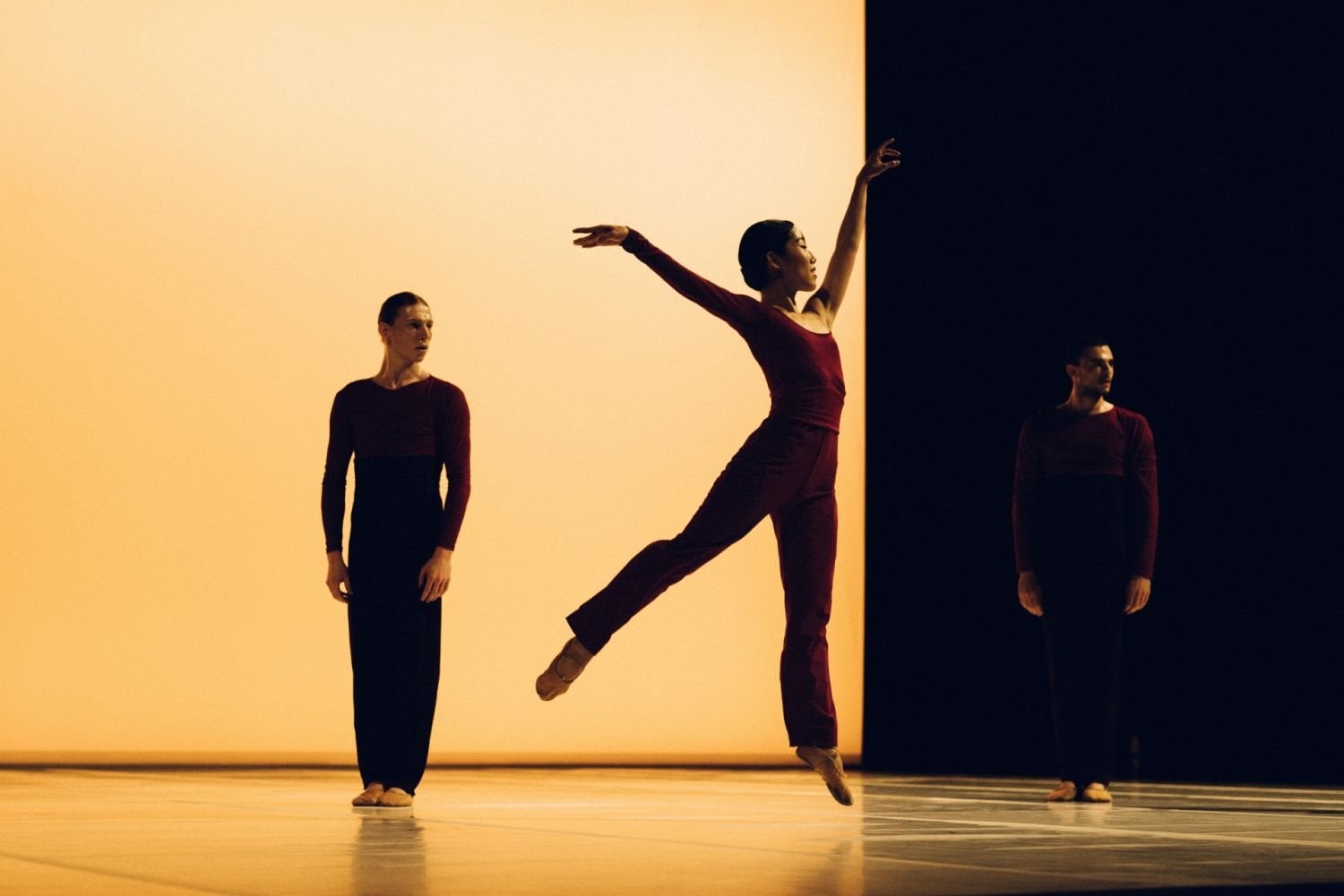 Leaping dancer in front of two static dancers on-stage 