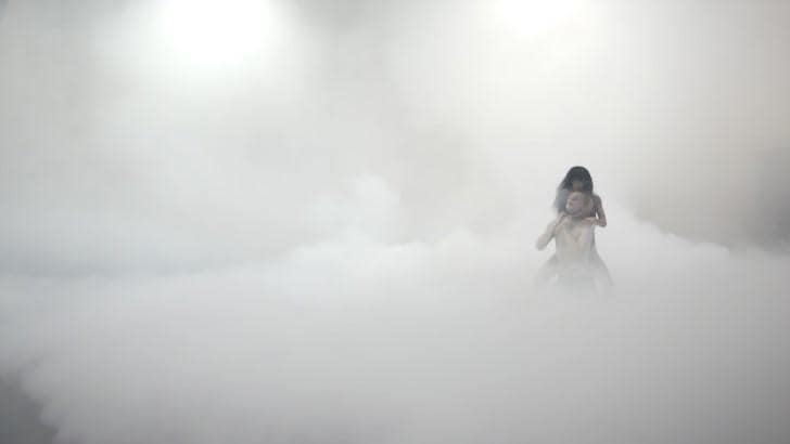 在霧氣籠罩的舞台中央，一位女性正在扼緊一位男性