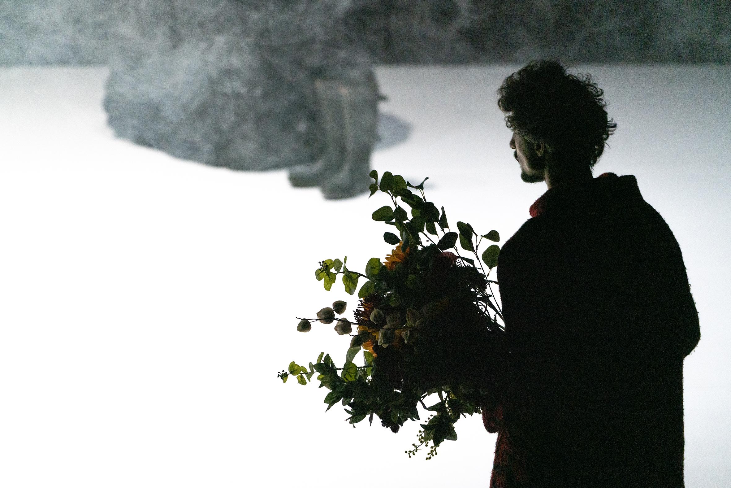 一个人手拿花束，站在雾蒙蒙的空间前