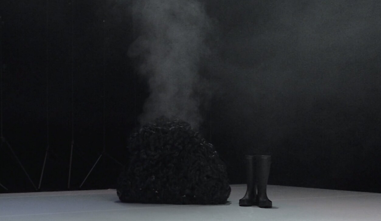暗淡的空间内，一个黑色雾状造型与中央一对黑色橡胶靴