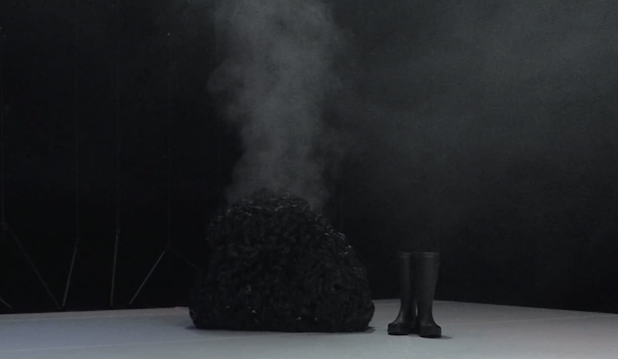 dark space with a black foggy shape and a pair of black rubber boots in the middle