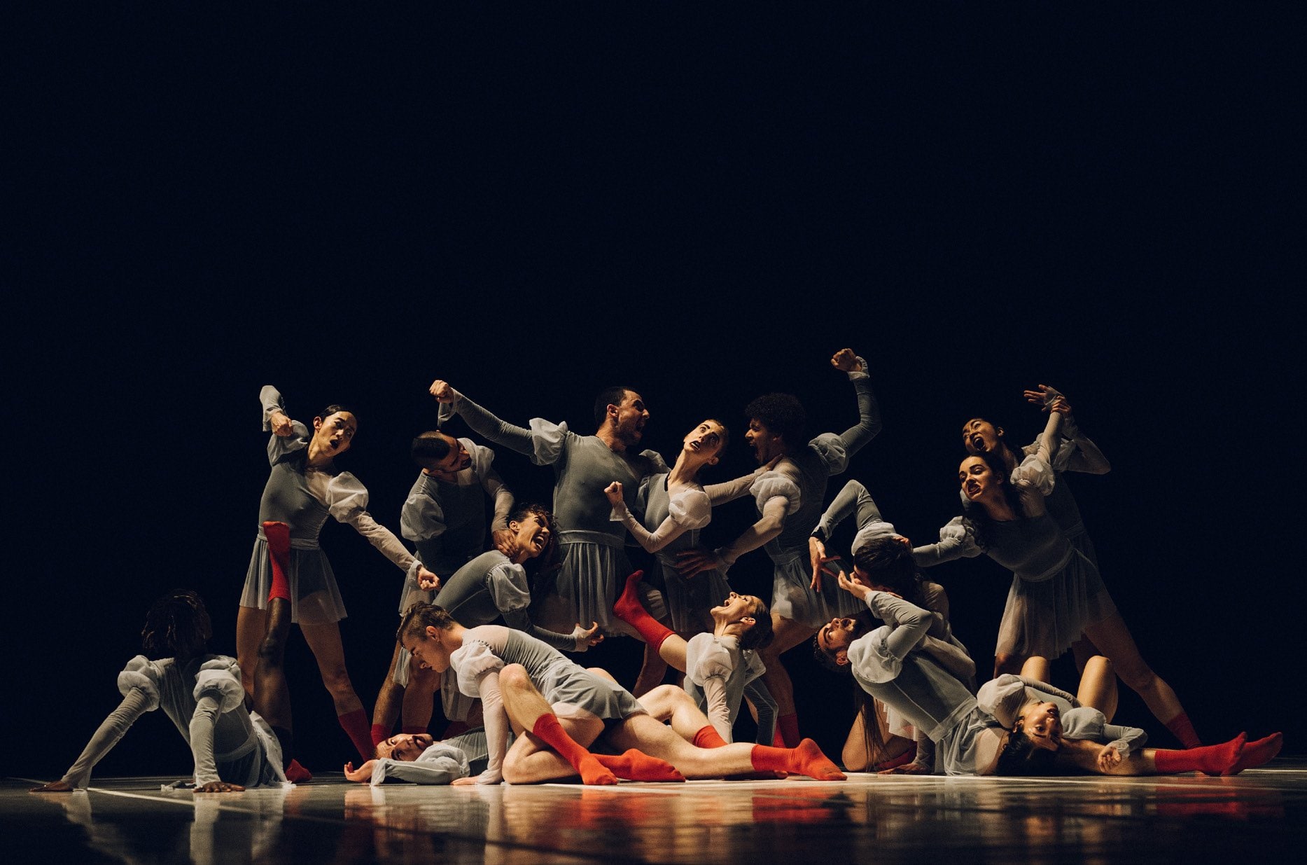 Group of dancers on-stage dressed in gray, with red socks