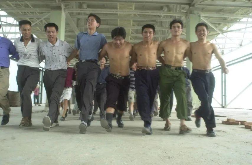 shirtless farmers in a line, holding each other by the waist