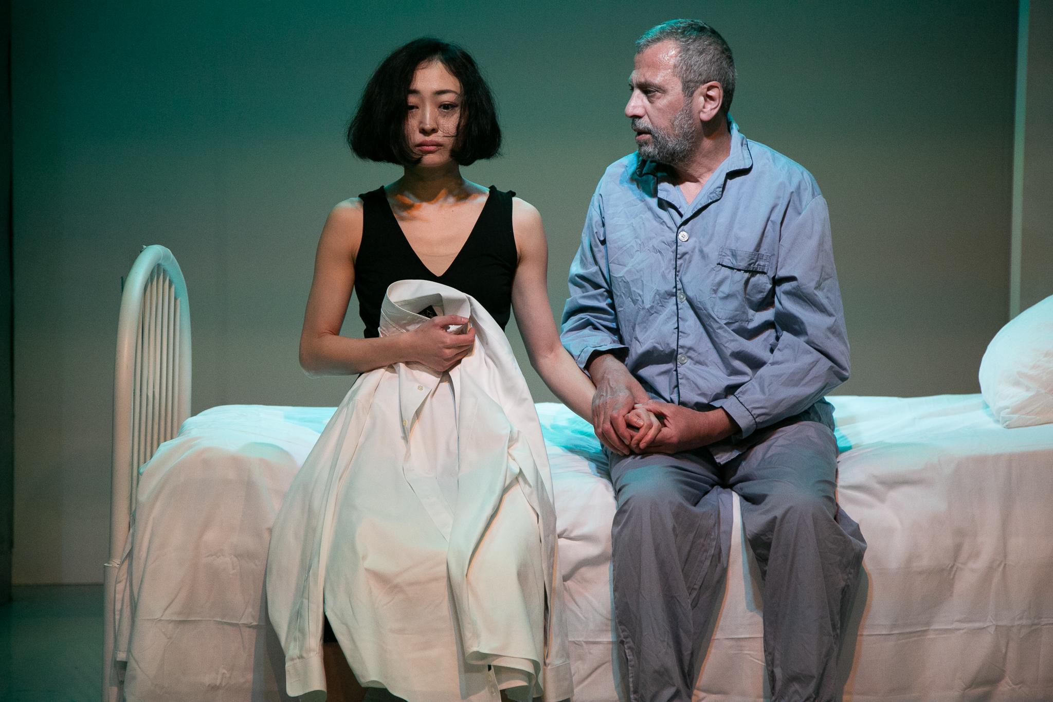 a man sitting on a hospital bed holding the hand of a woman sitting next to him