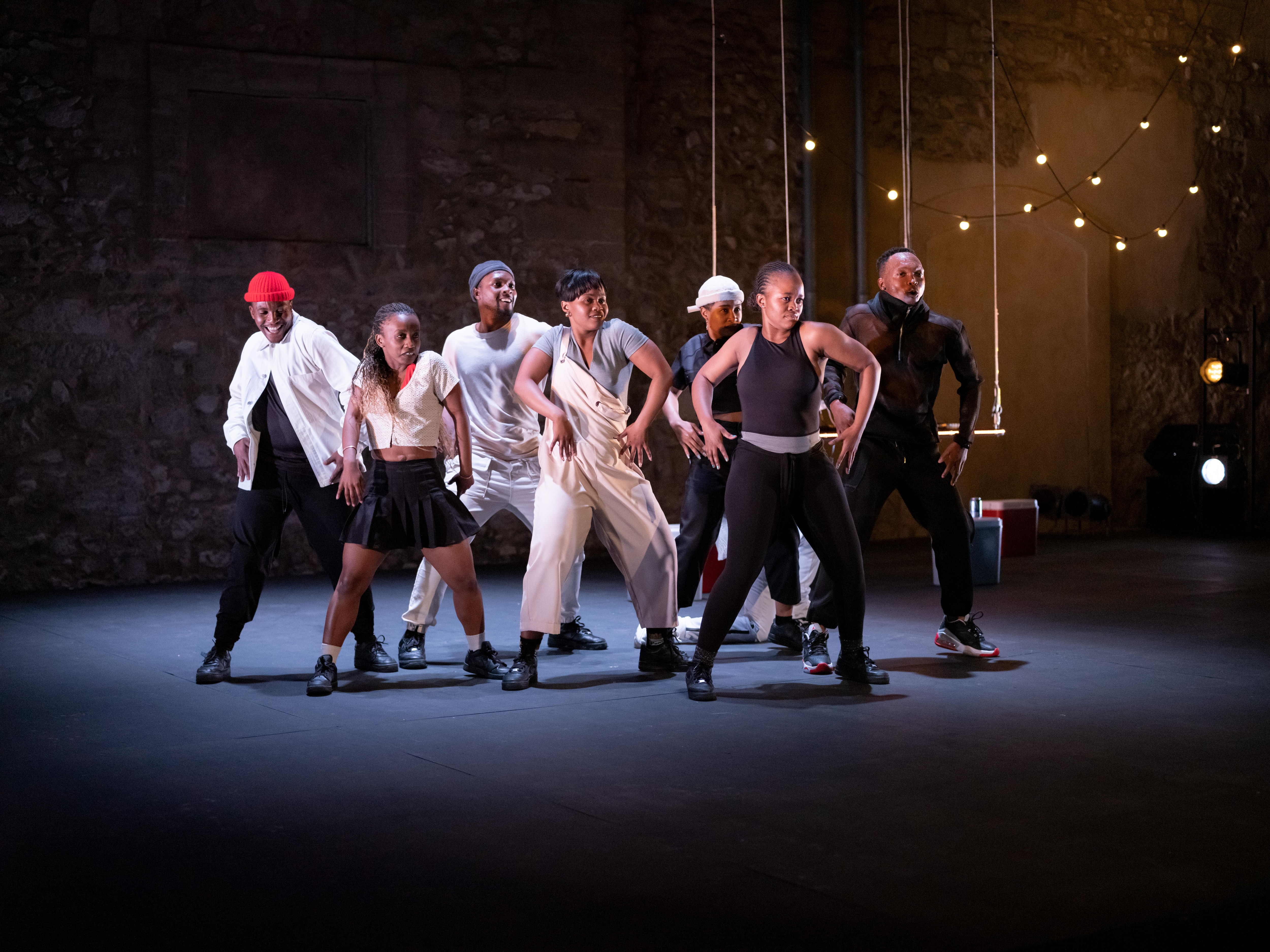 Group of dancers, in front, on a dark stage, arms and legs spread