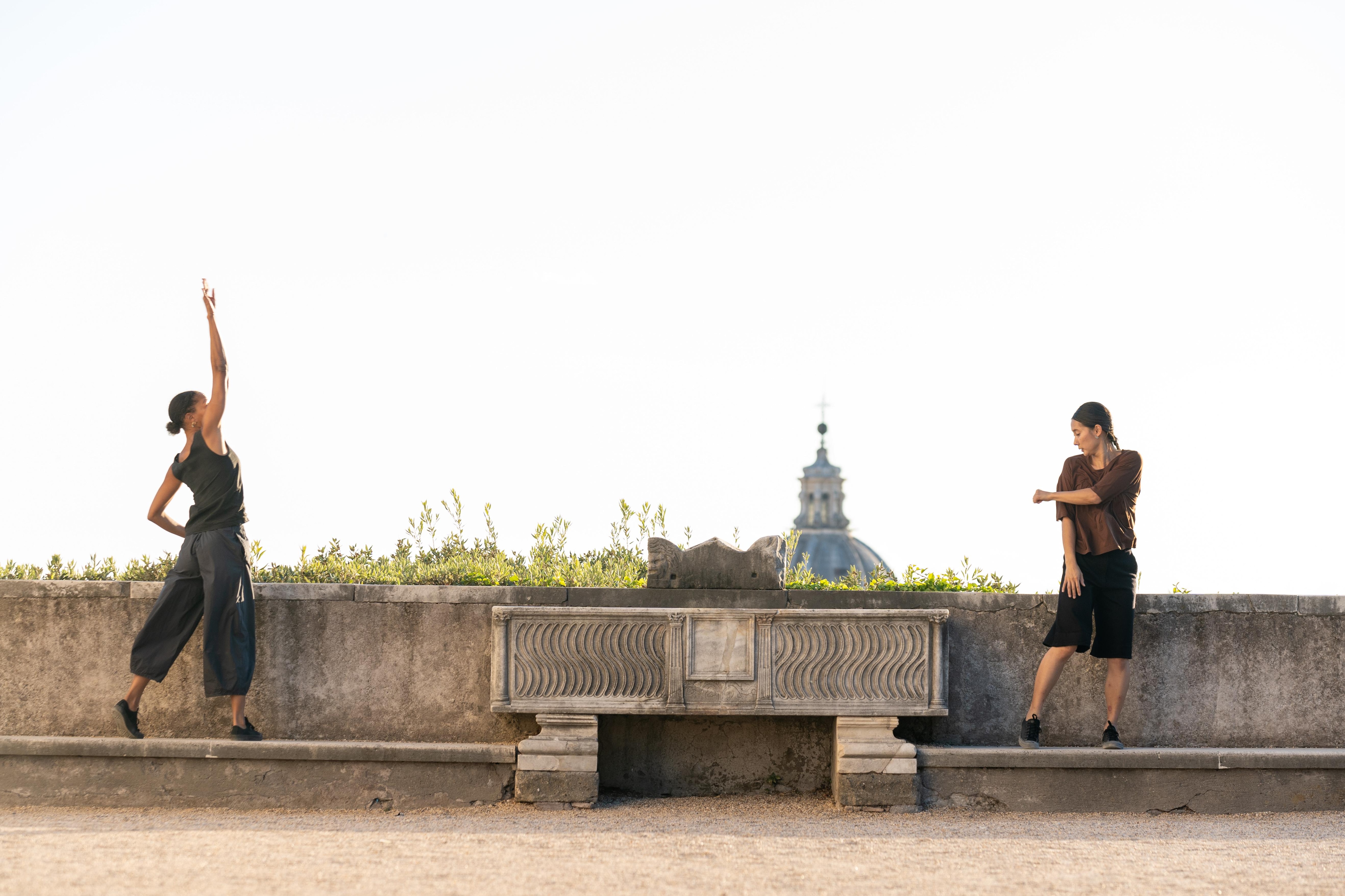 兩位舞者面對面地站在一堵低矮的水泥牆上