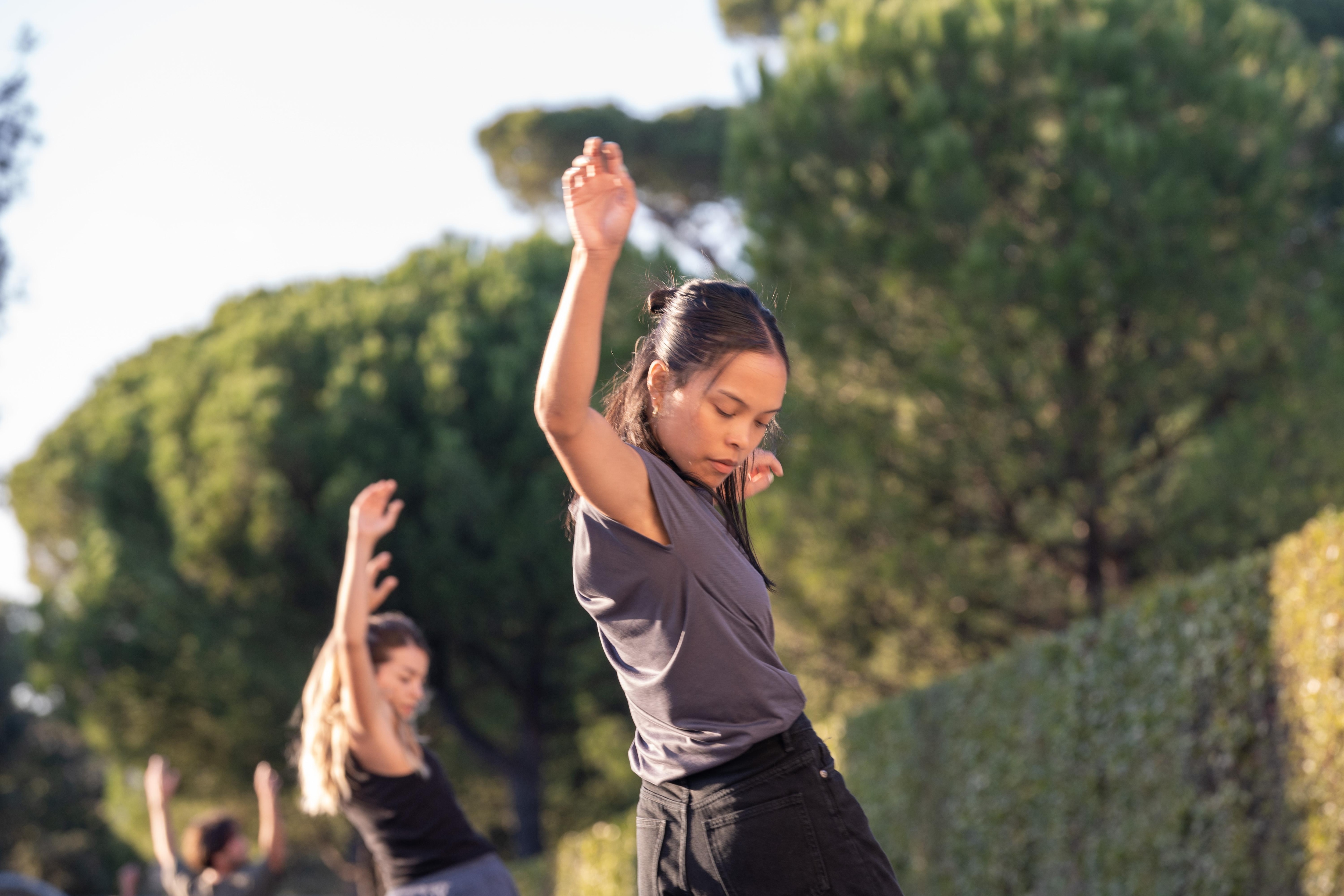 Danseuse vêtue de noir, le bras droit en l’air et regardant vers le sol dans les jardins de la Villa Médicis