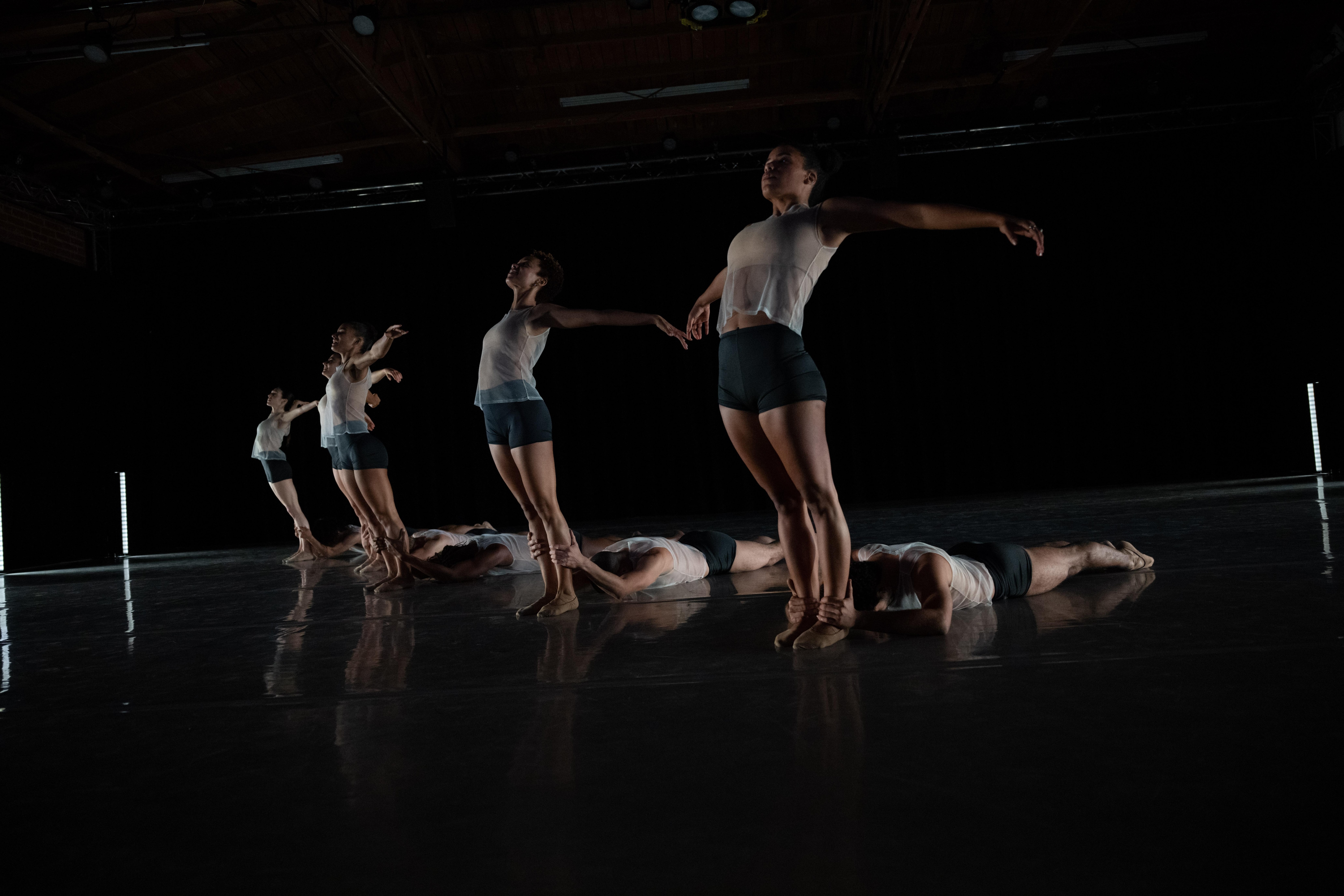 danseurs allongés sur le sol retenant par les chevilles des danseuses cambrées vers l’arrière, les bras écartés.