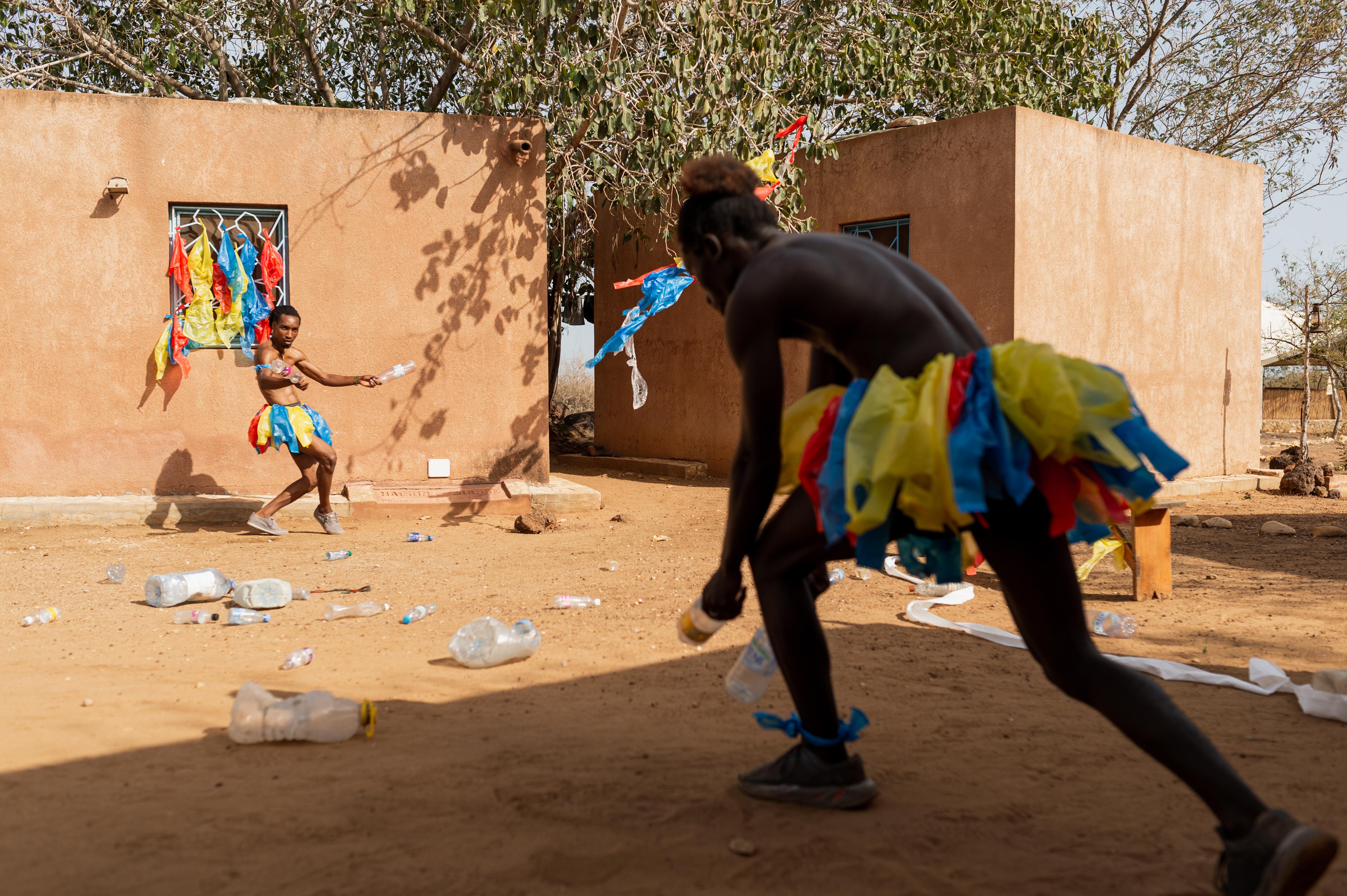 Two dancers holding empty plastic bottles, dancing on a floor littered with plastic bottles