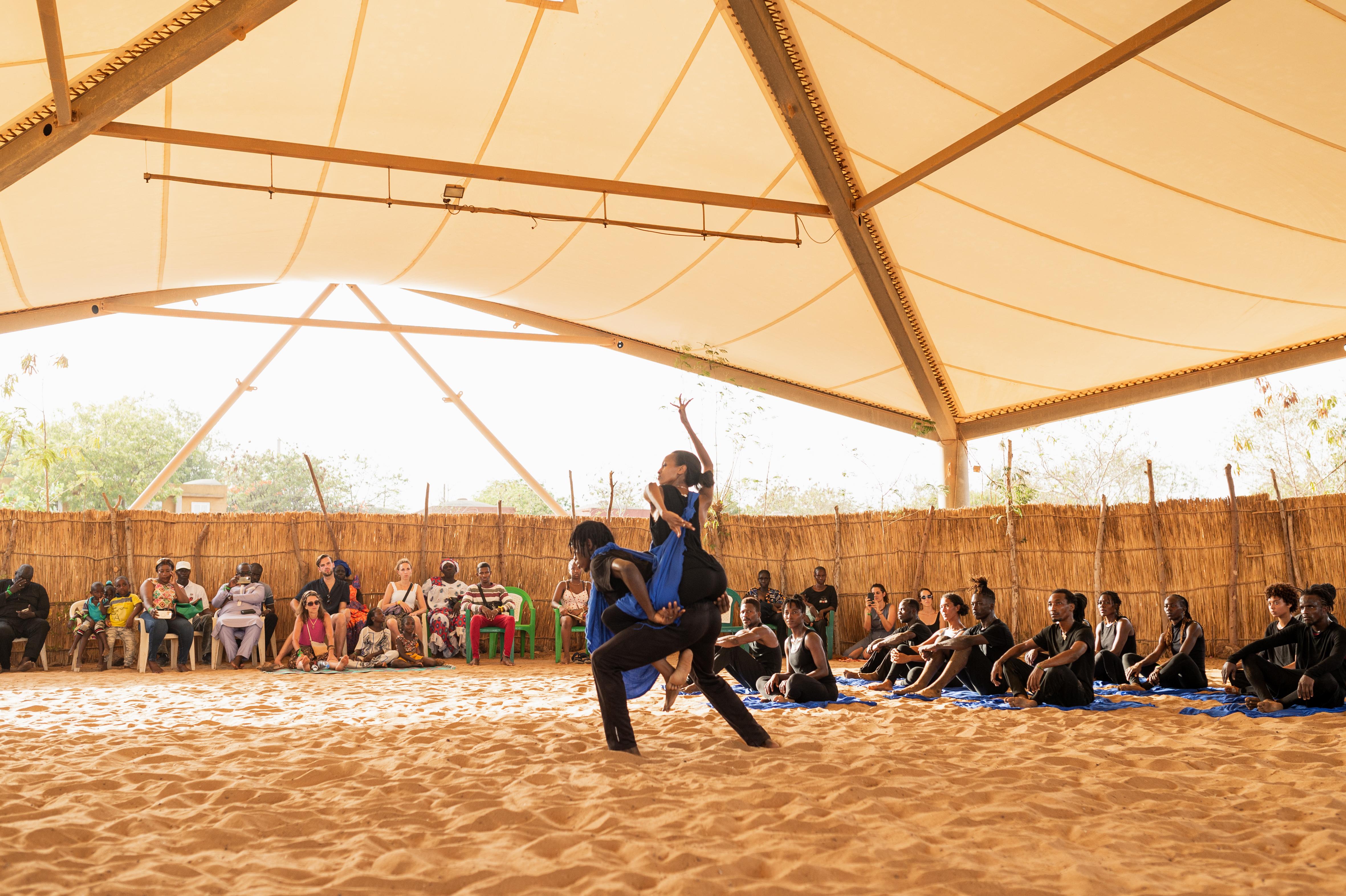 Un danseur porte une danseuse sur son dos, dans une arène avec des spectateurs 