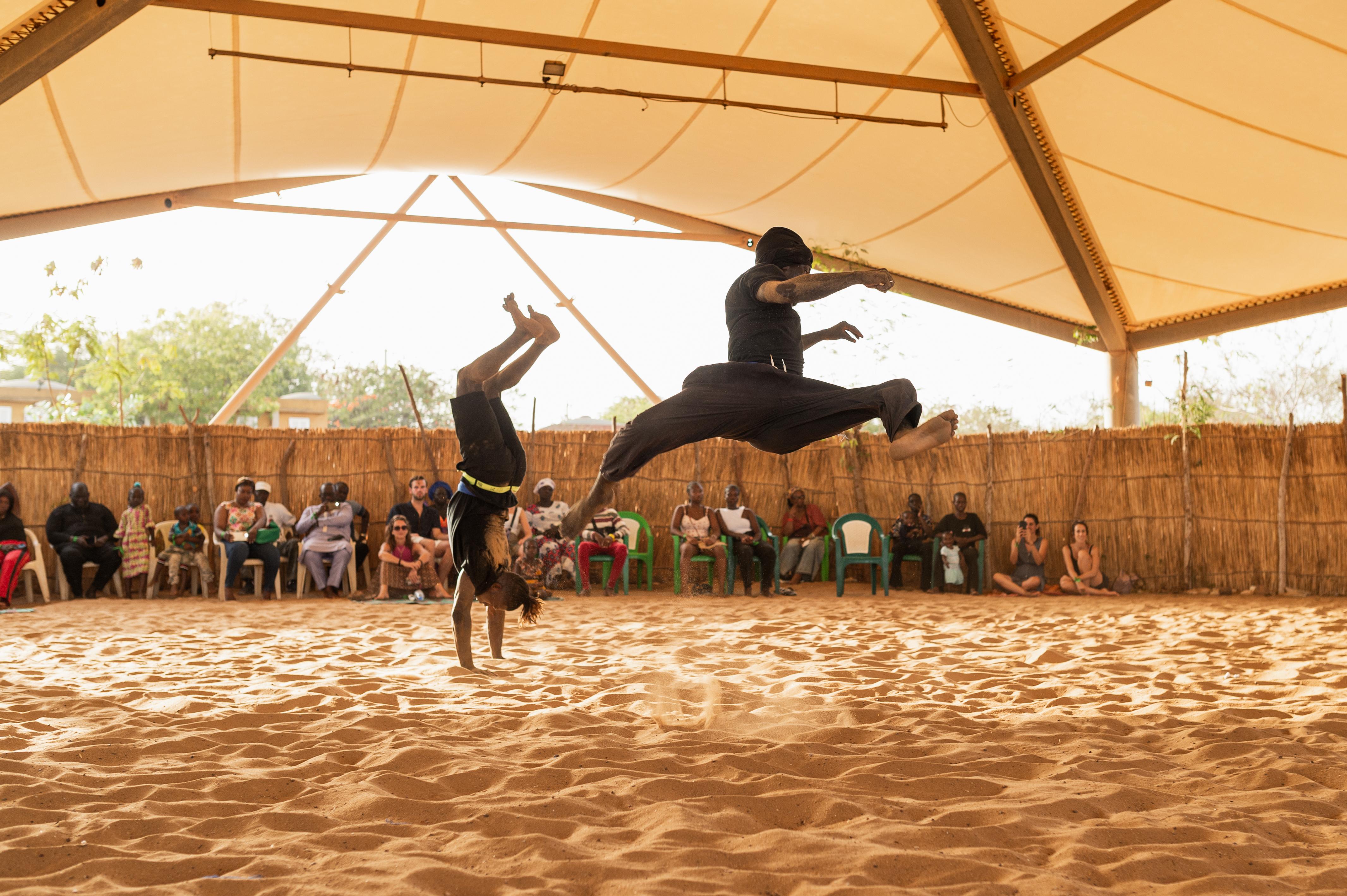 A dancer doing a headtand, and another one is jumping in the air