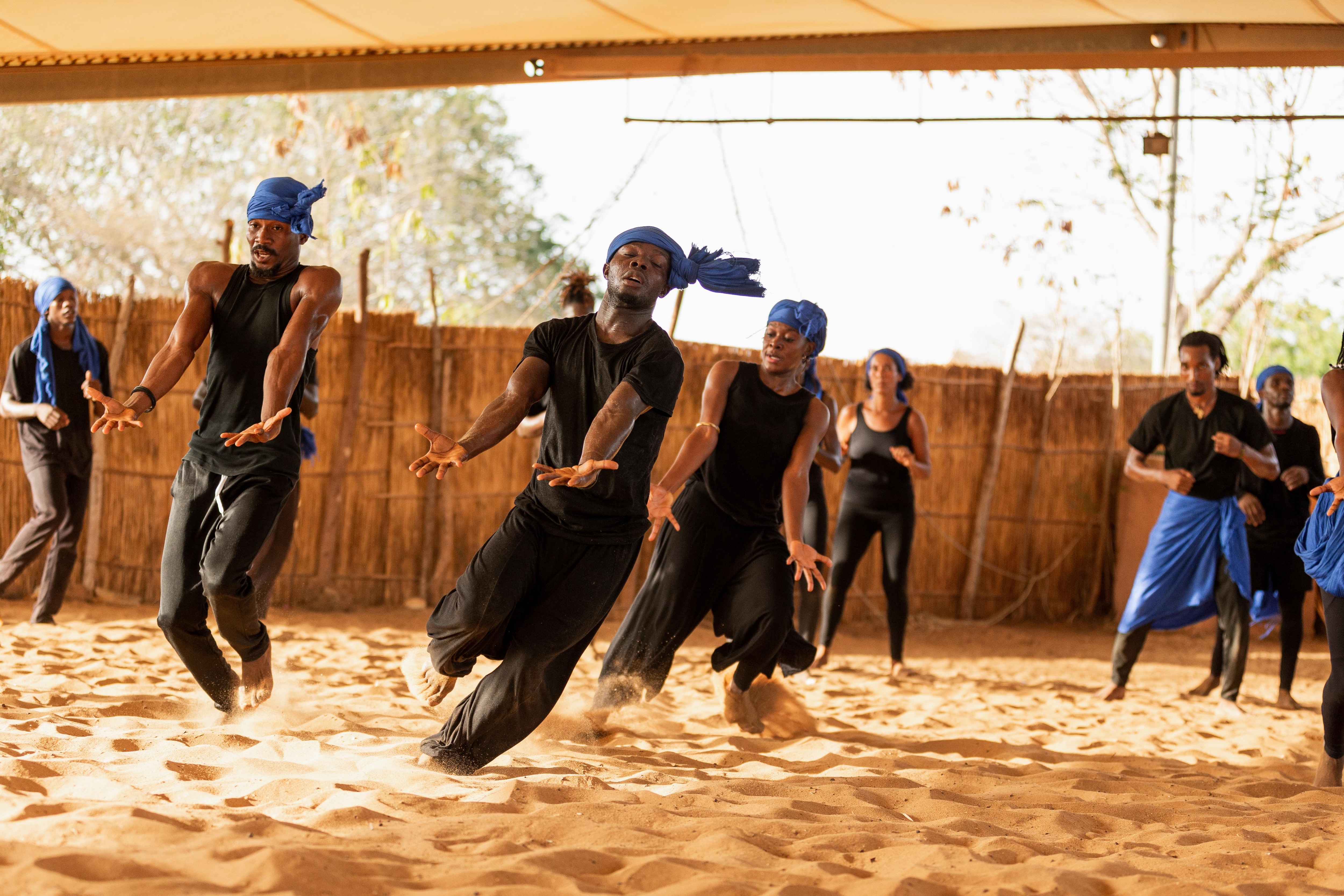 Dancers in movement with a blue scarf on their head, hands opened in front of them
