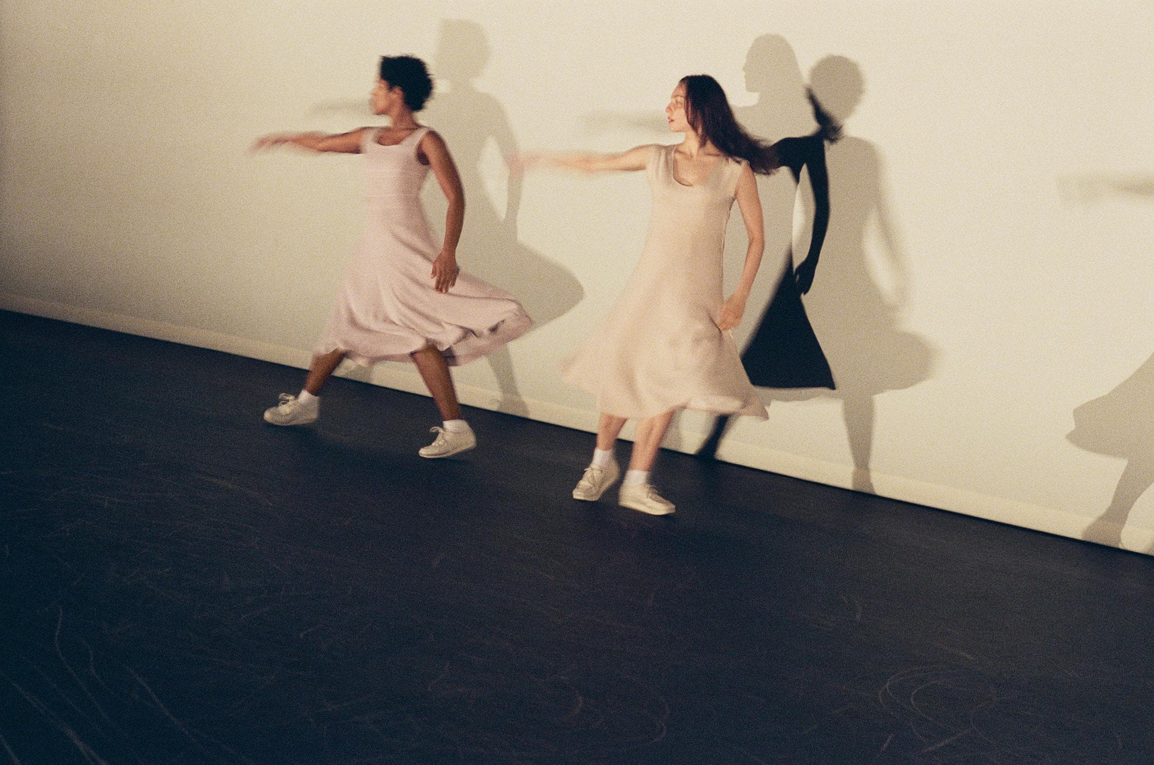 Two dancers and their shadow, right arms extended 