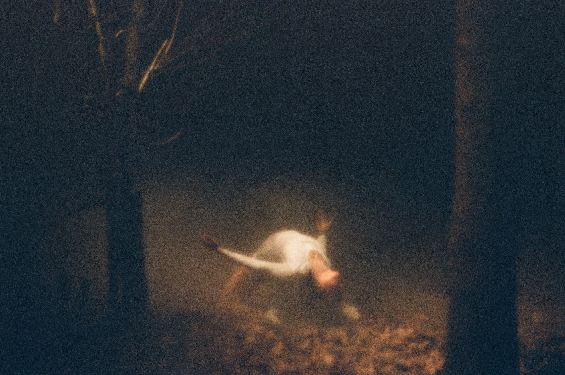 Dancer bent over, chest up, on a floor of leaves, surrounded by trees