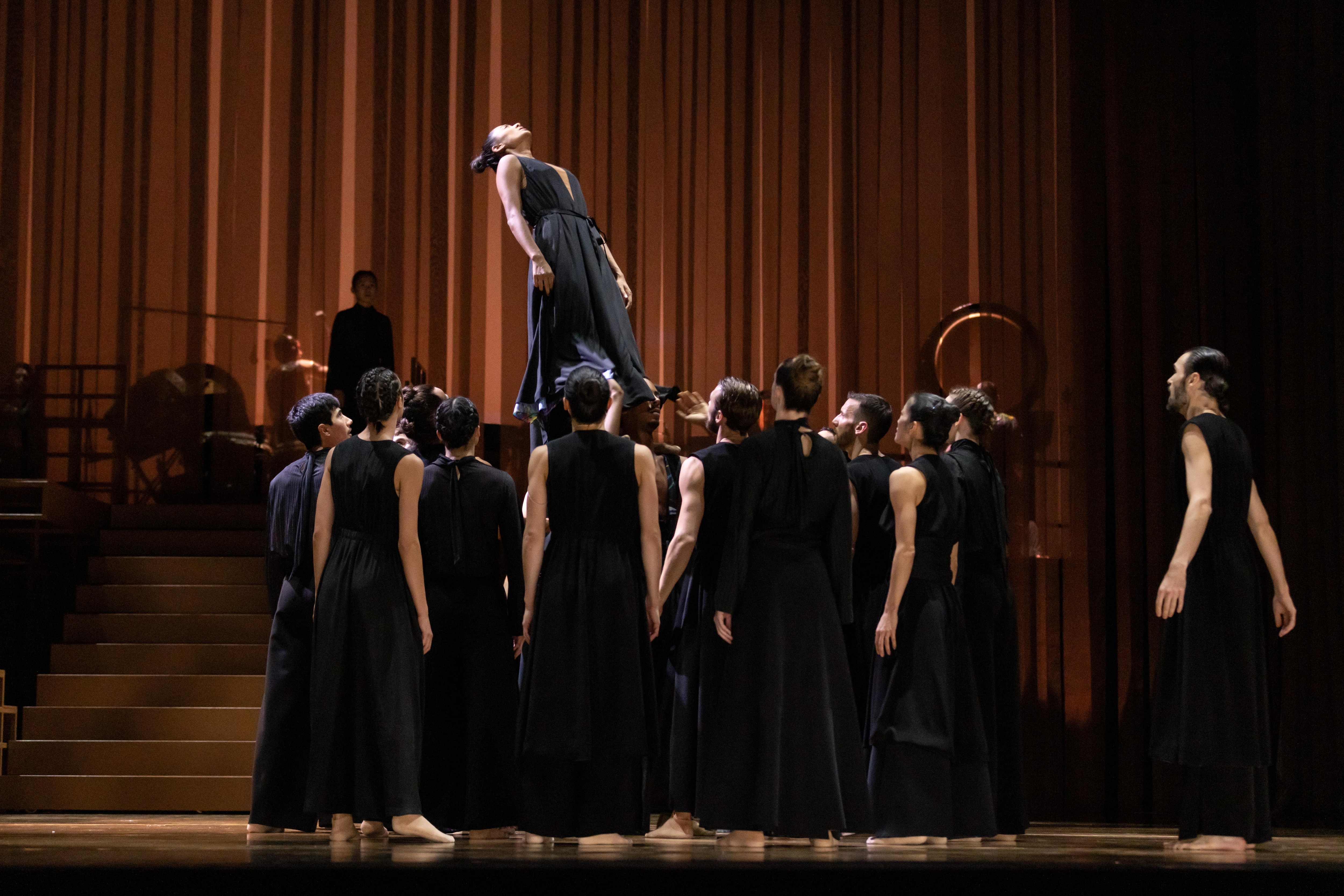 Danseurs de Ukiyo-e par Sidi Larbi Cherkaoui en costume noir. Ils font cercle autour d’un danseur porté vers le haut.